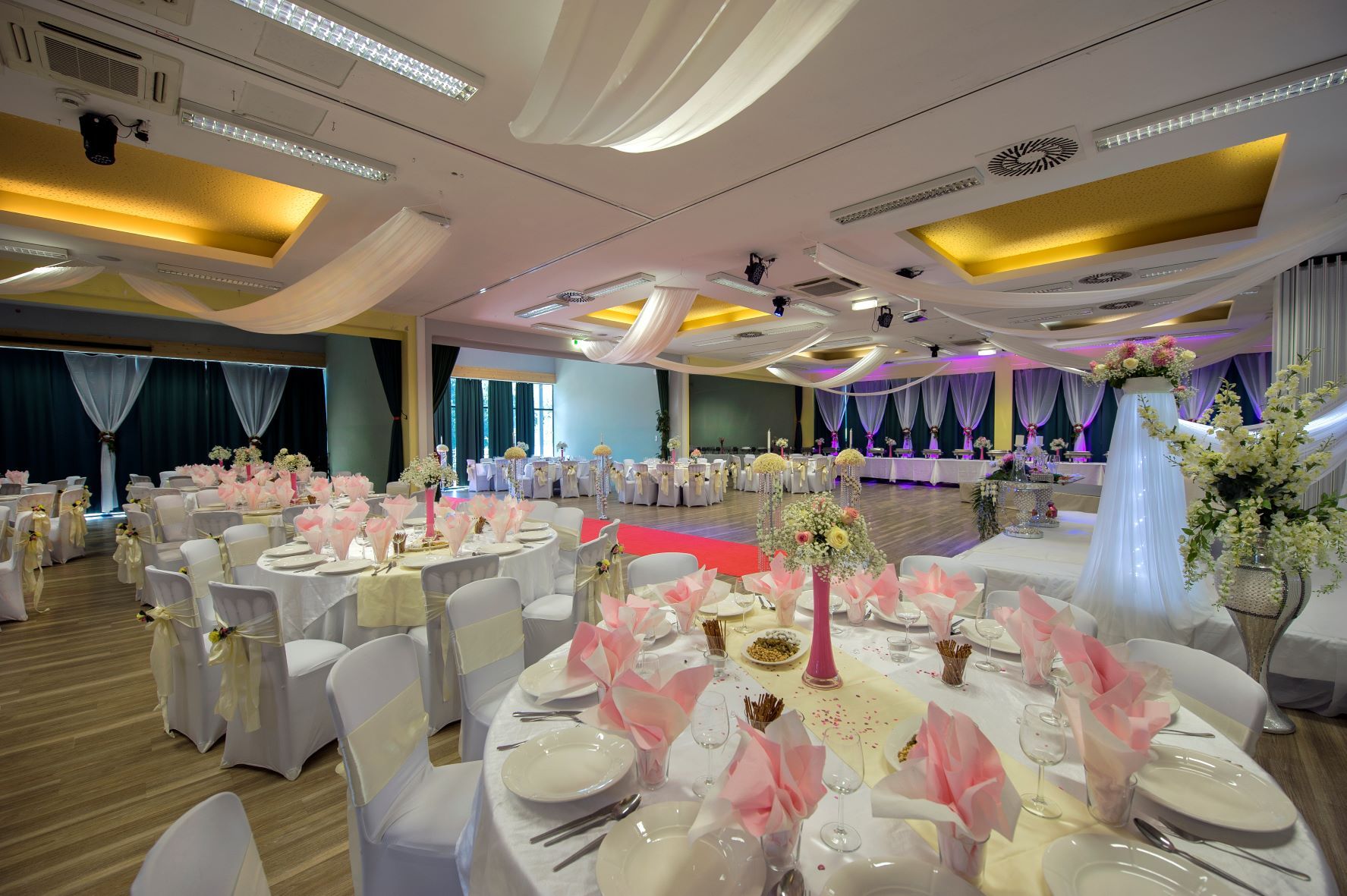 Large banqueting hall with many tables and a laid table. 