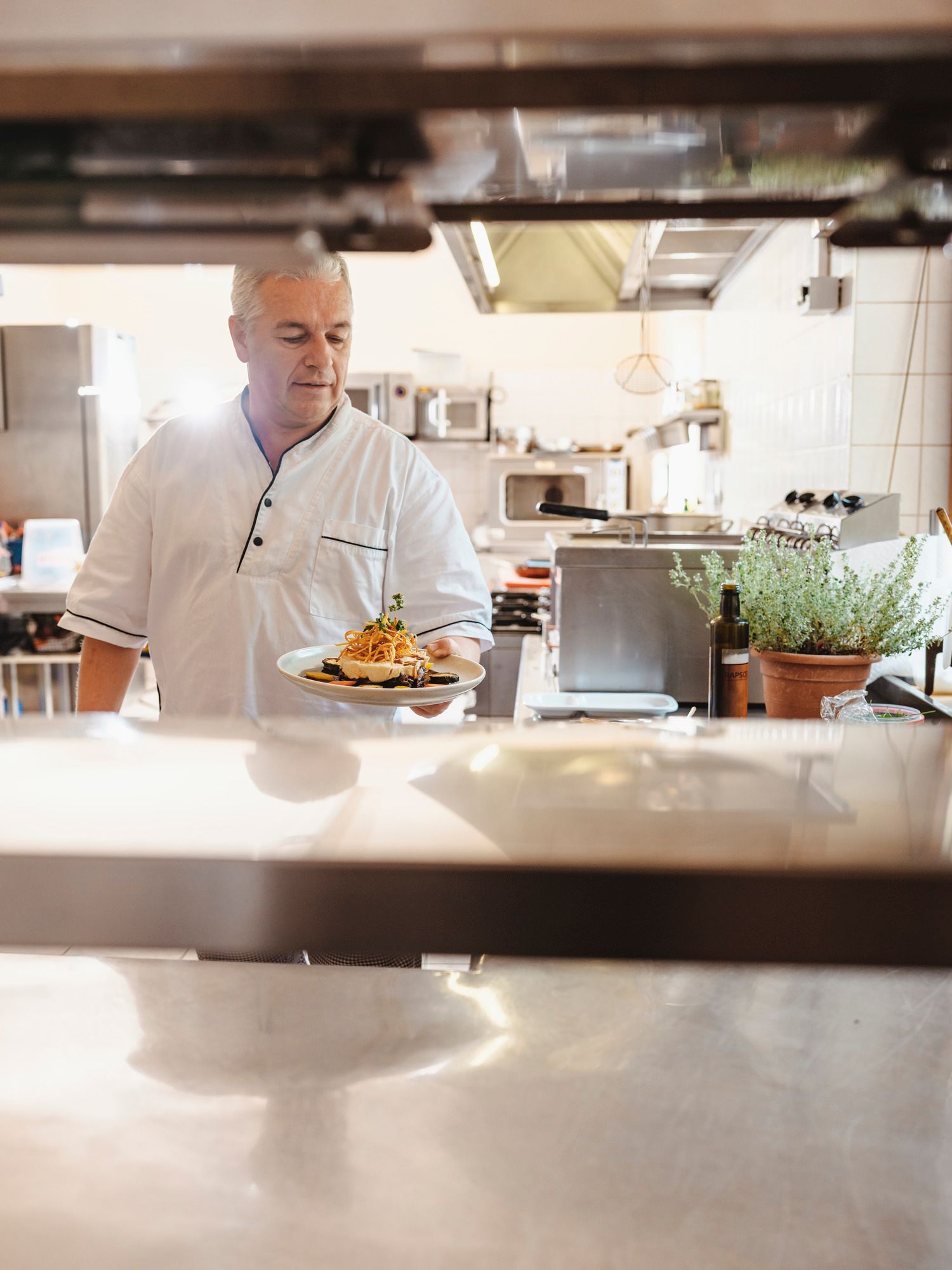 A cook in a restaurant kitchen holds a plate of food in his hand.