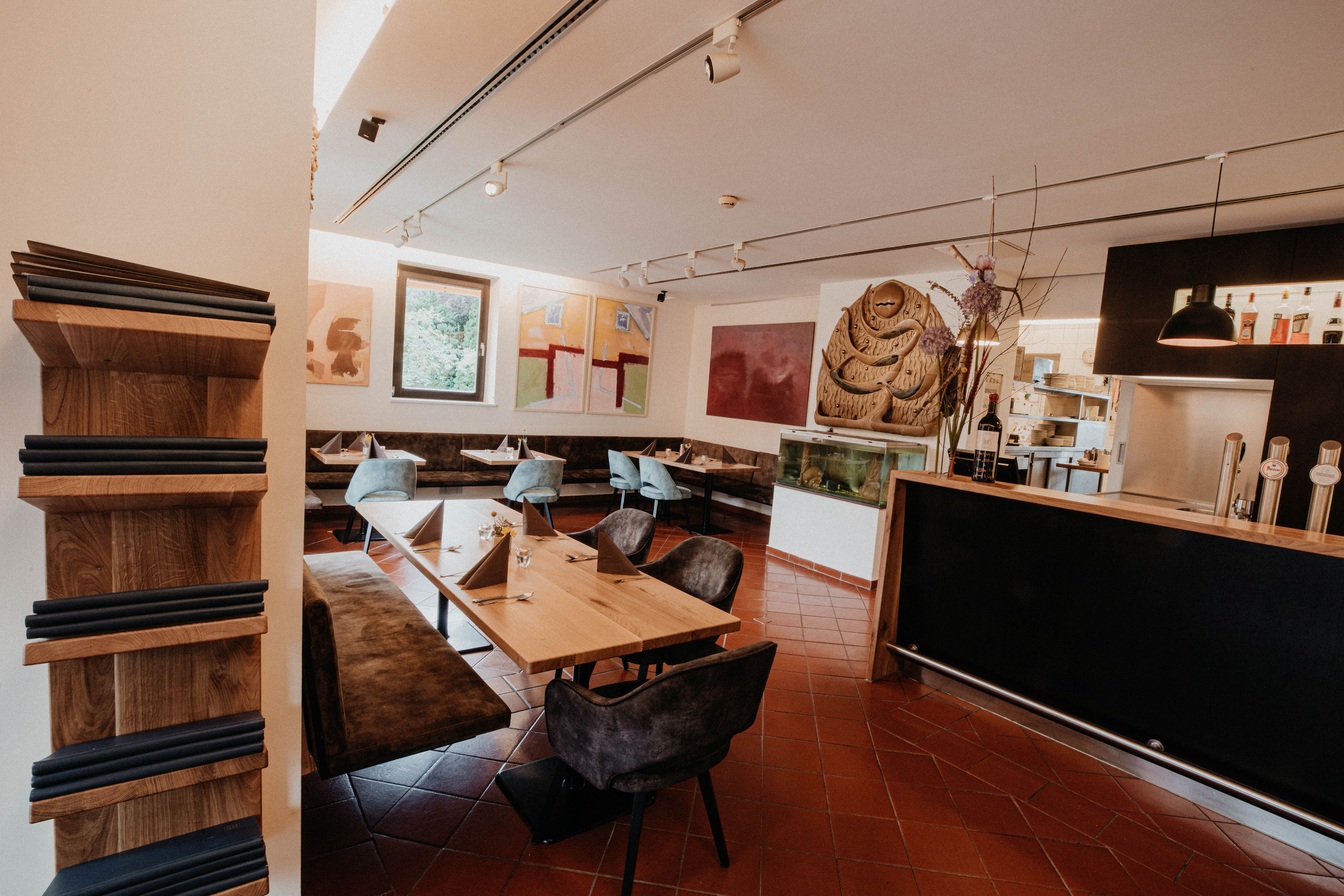 Interior view of a modern restaurant with wooden tables, blue chairs and works of art on the walls.