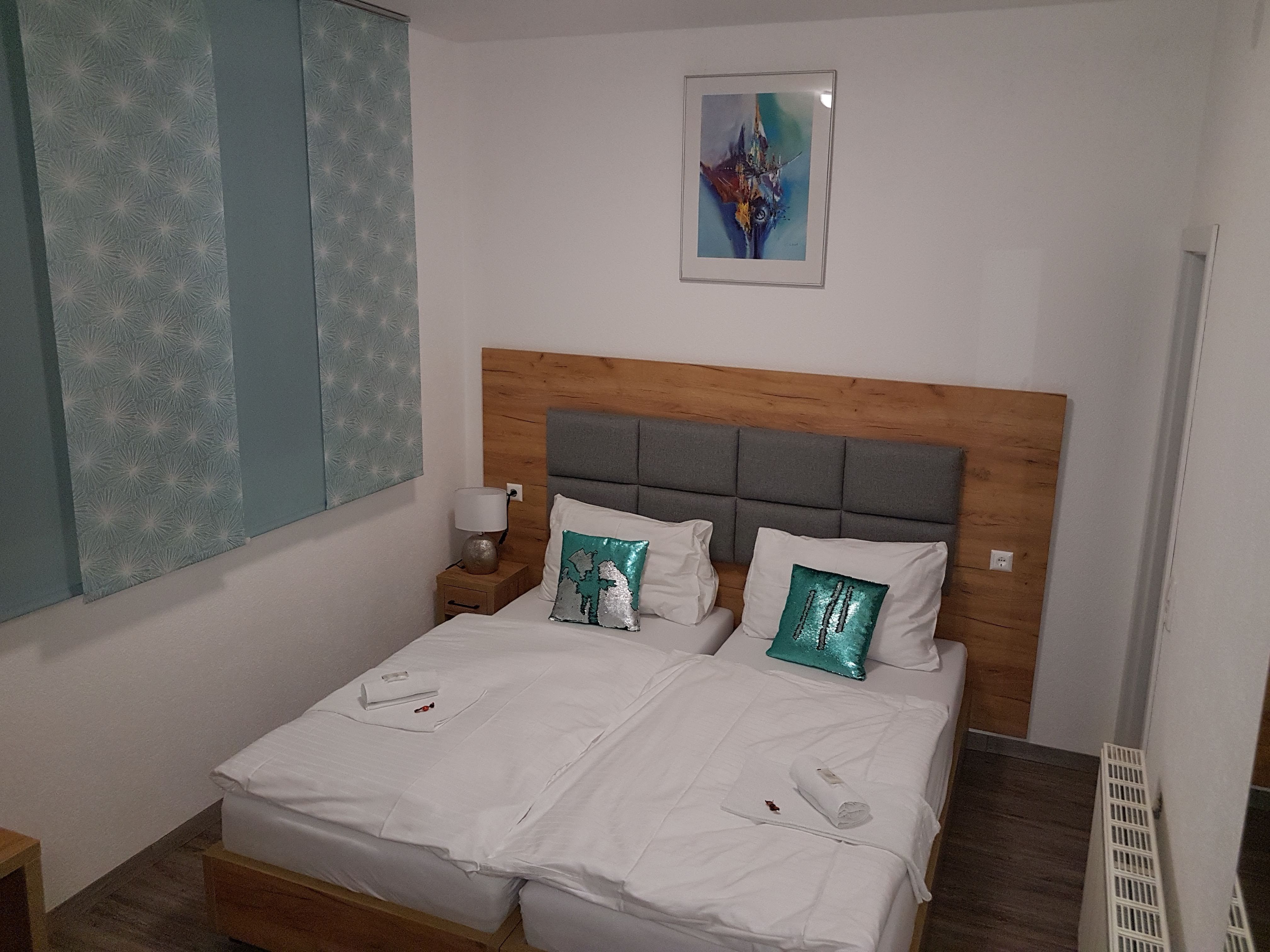 Double room with two single beds, wooden headboard, decorative cushions and a picture on the wall.