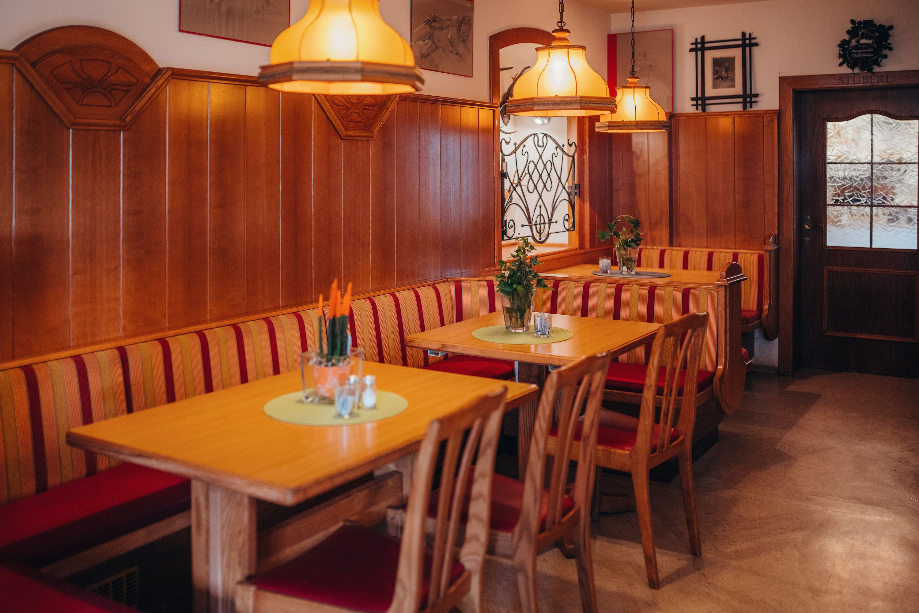 Cozy dining room with wooden furniture and red upholstery, decorated with plants and warm light.