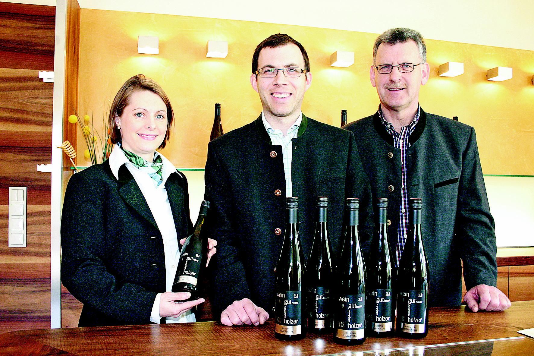 Three people stand behind a table with bottles of wine in the Holzer winery.