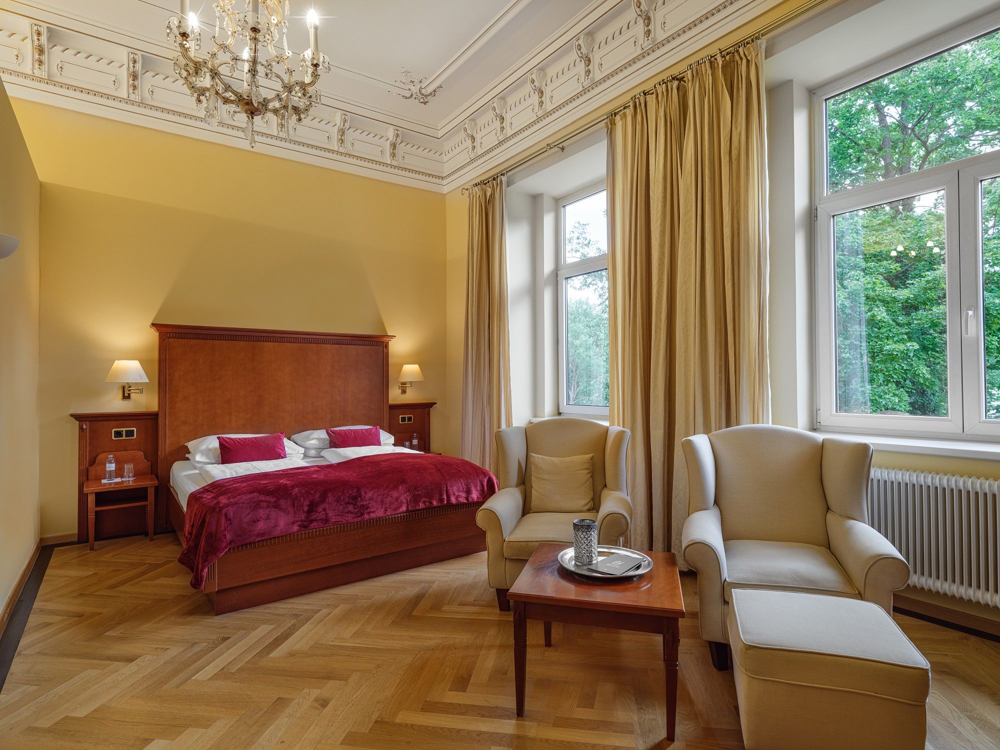 Elegant hotel room with double bed, armchairs and large windows.