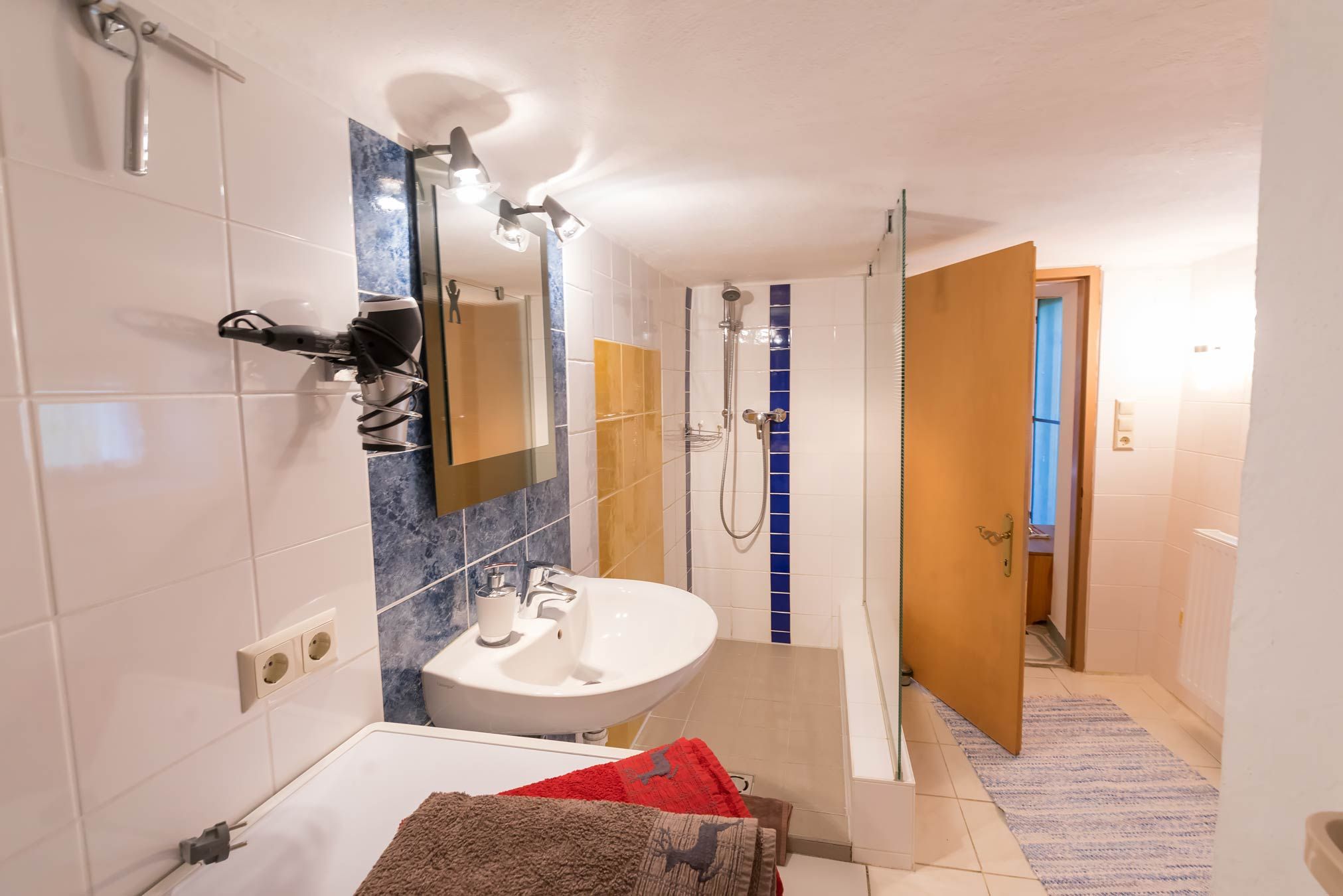 A bathroom with washbasin, mirror, shower and towels.