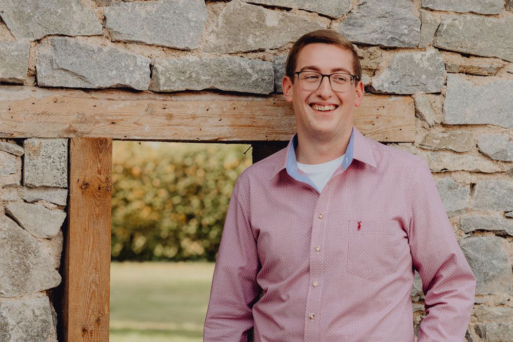 Man in pink shirt leaning against a stone wall.