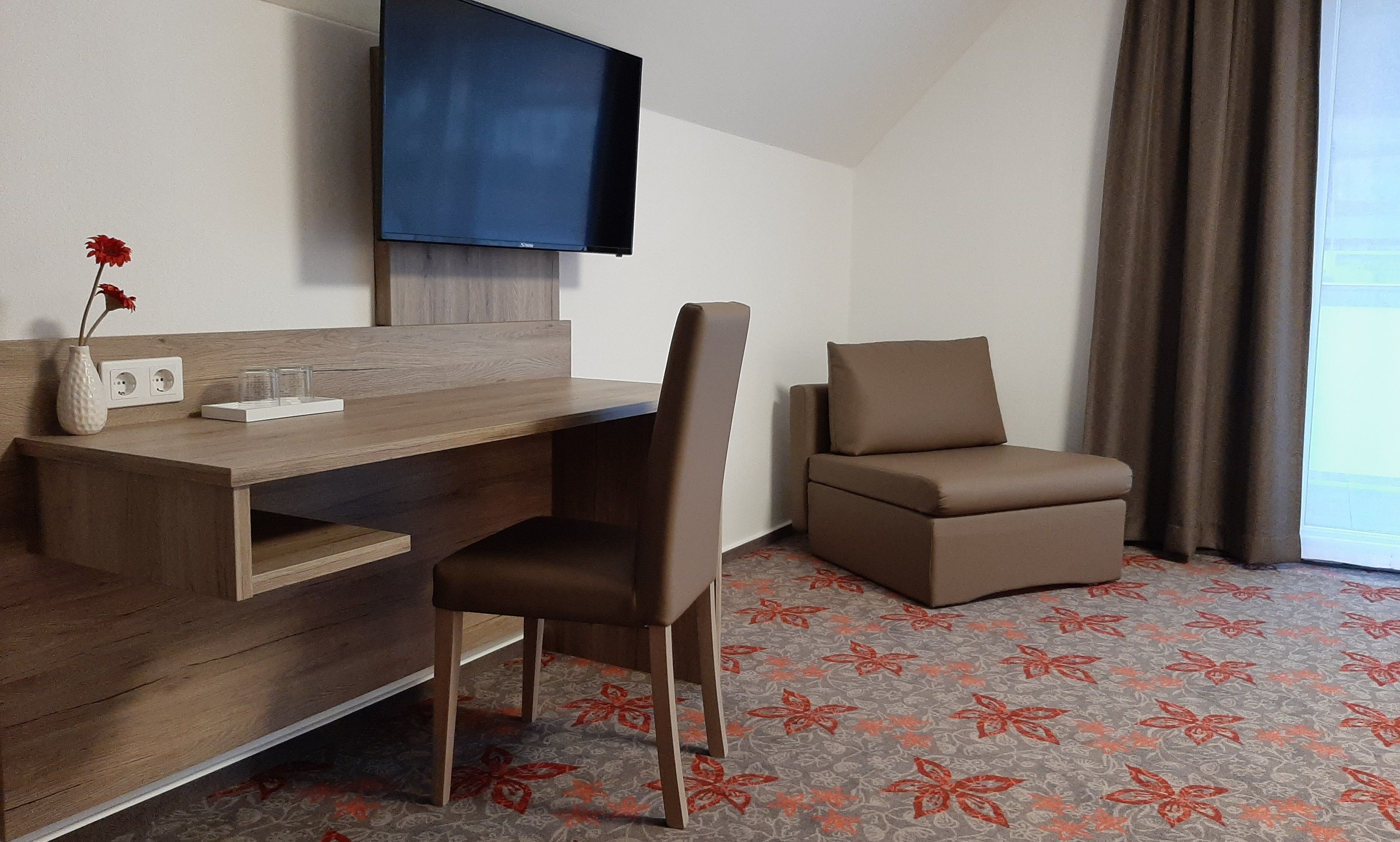 Hotel room with desk, chair, TV and armchair.