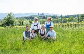 A family in traditional dress poses in a meadow with a castle in the background.