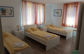 Three single beds in a bright room with yellow bed linen and colorful curtains.