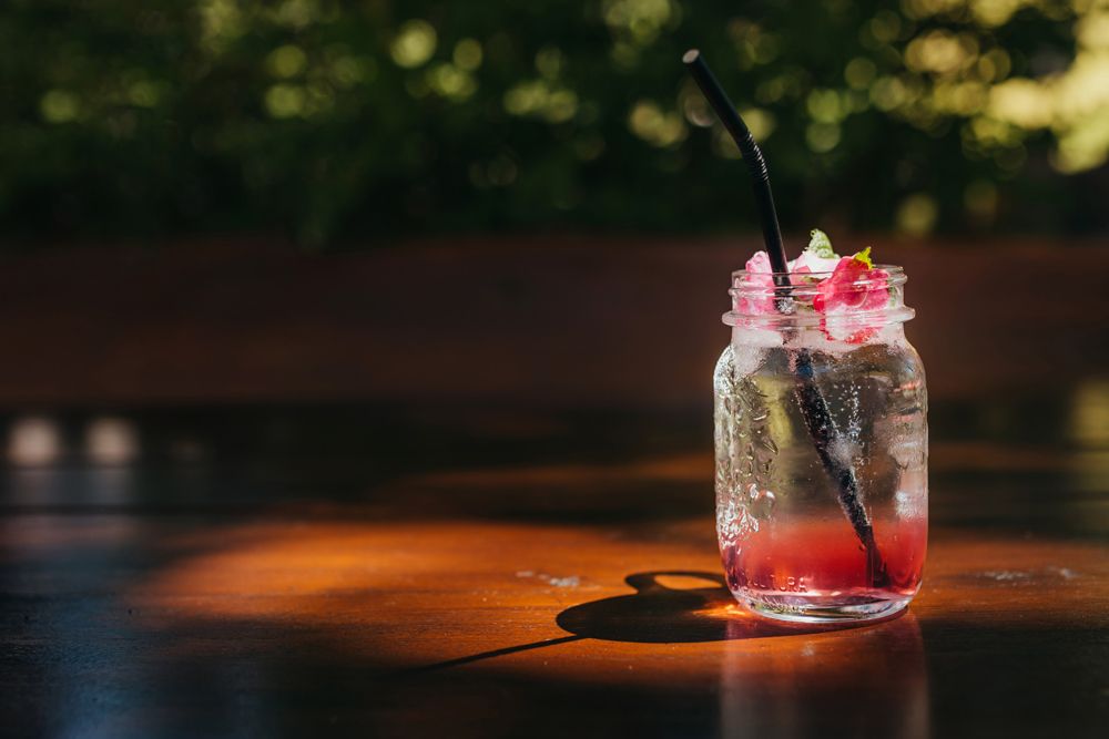 A glass with a red drink and a black straw on a wooden table.