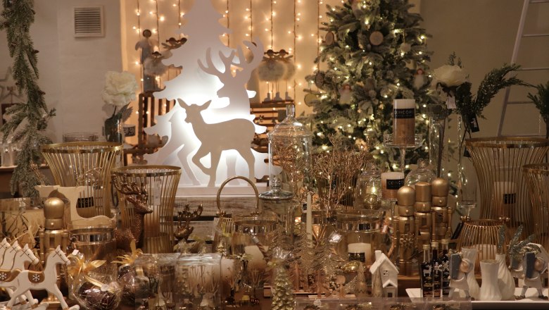 Christmas decorations with gold and white elements, including candles, reindeer and a Christmas tree in the background.