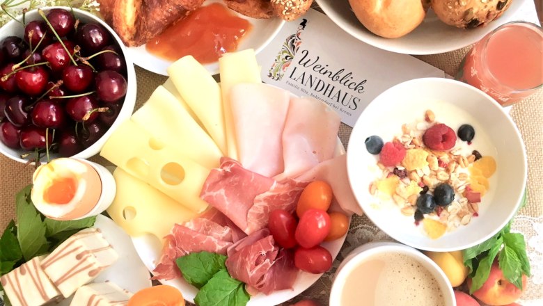 A rich breakfast with cheese, ham, croissants, fruit, muesli, egg and coffee on a table.