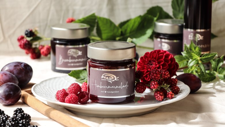 A jar of raspberry jam on a plate decorated with fresh berries and flowers.