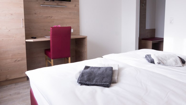 Double room with bed, desk, chair and TV on the wall.