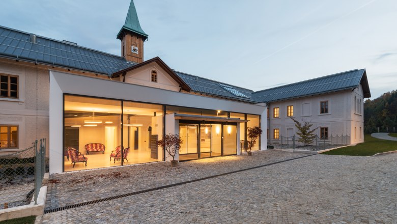 Refugium Hochstrass, © Andreas Buchberger Modern building with glass façade and historic tower in the background.