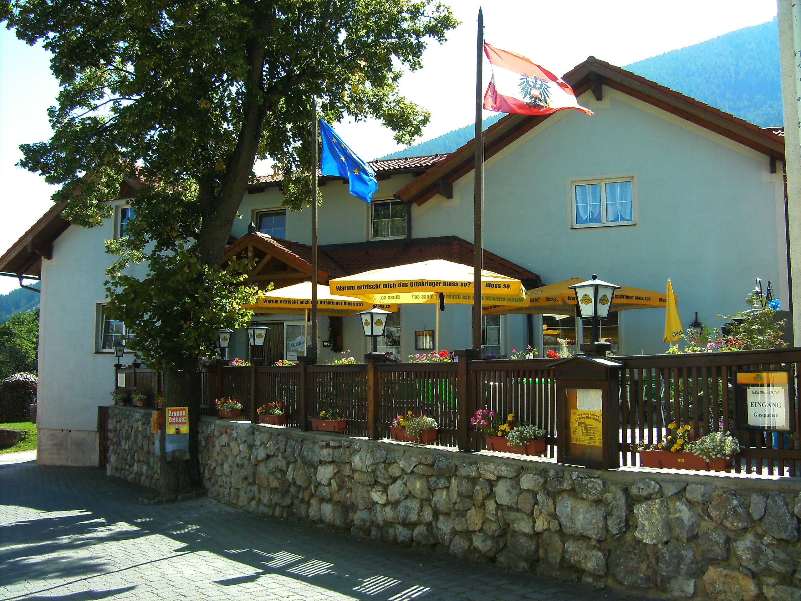 Gasthof Zwinz with terrace and parasols, surrounded by flowers and flags.