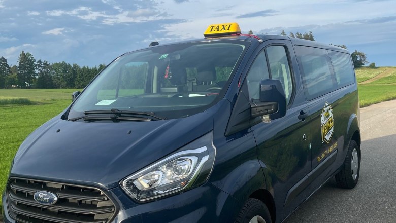 A blue Ford cab is parked on a country road in front of a green meadow and a cloudy sky.