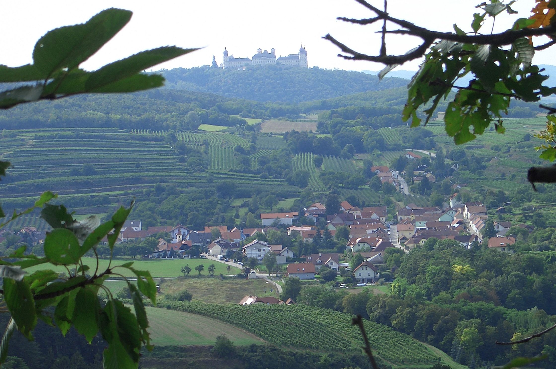 View of Göttweig Abbey on a hill, surrounded by vineyards and a village in the foreground.