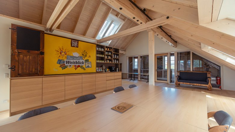 Interior view of a modern loft with wooden beams, large table and shelves.