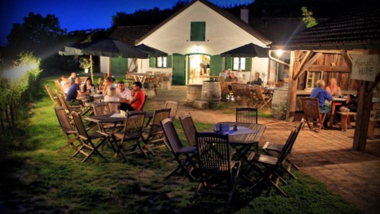 Evening scene in a wine tavern with guests at wooden tables outdoors.