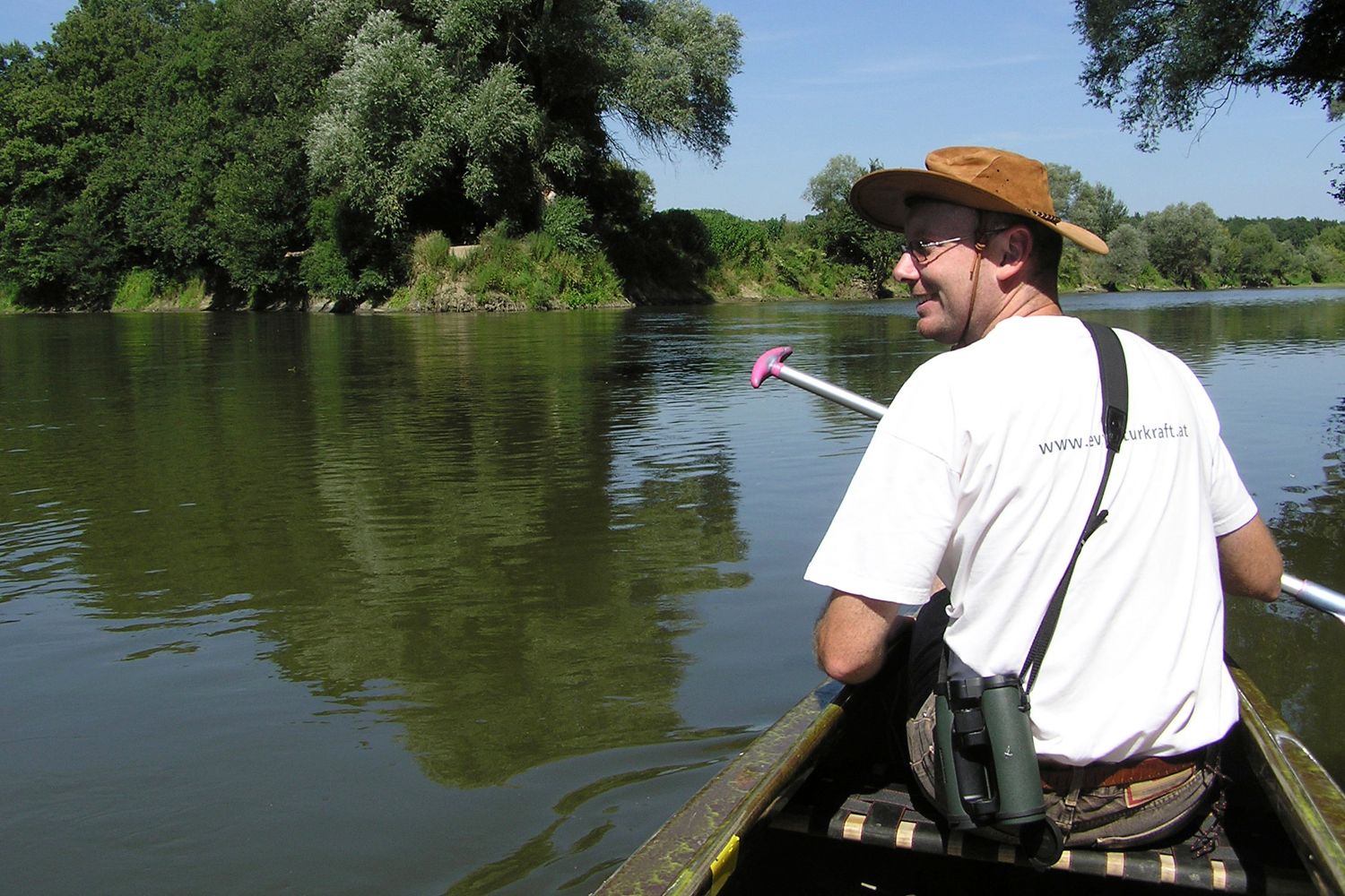 Person in a canoe on a river, surrounded by trees.