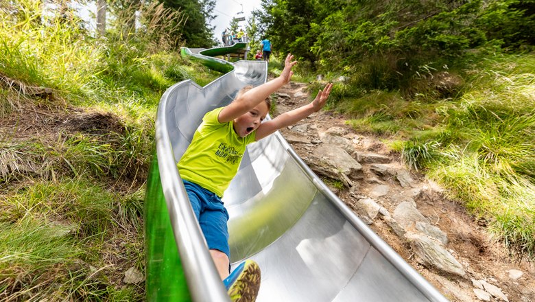Child sliding down a metal slide outdoors.
