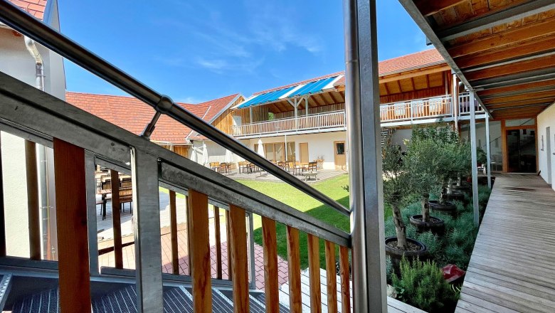 Inner courtyard with wooden veranda and plants, surrounded by buildings with red roofs.