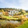 A hotel in the middle of a green landscape with a pond and sun loungers.