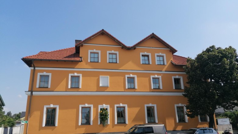 Bed and breakfast Csenar, © Wiener Alpen Yellow building with red roof tiles and several windows, cars parked in front of it and a tree.