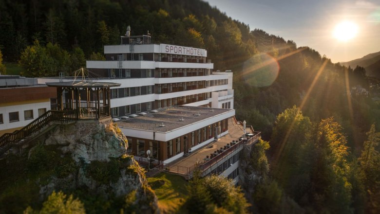 A hotel on a hill at sunset, surrounded by forest.