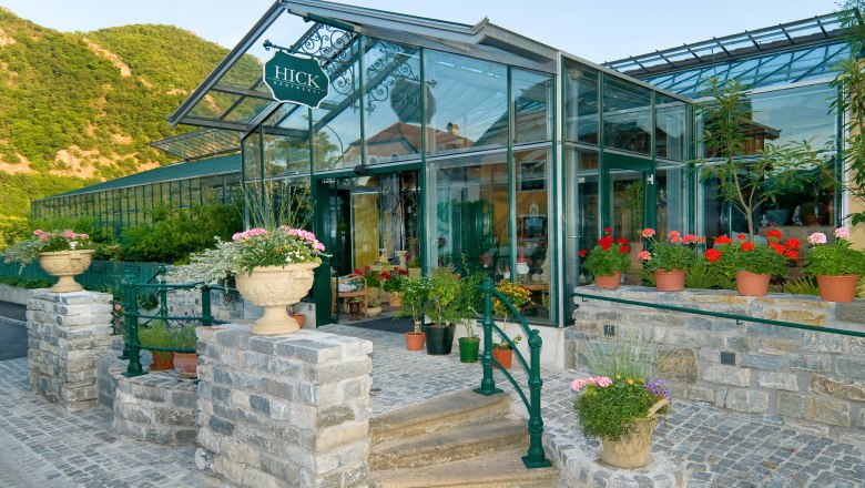 Entrance to a nursery with a glass roof and flowers in pots.