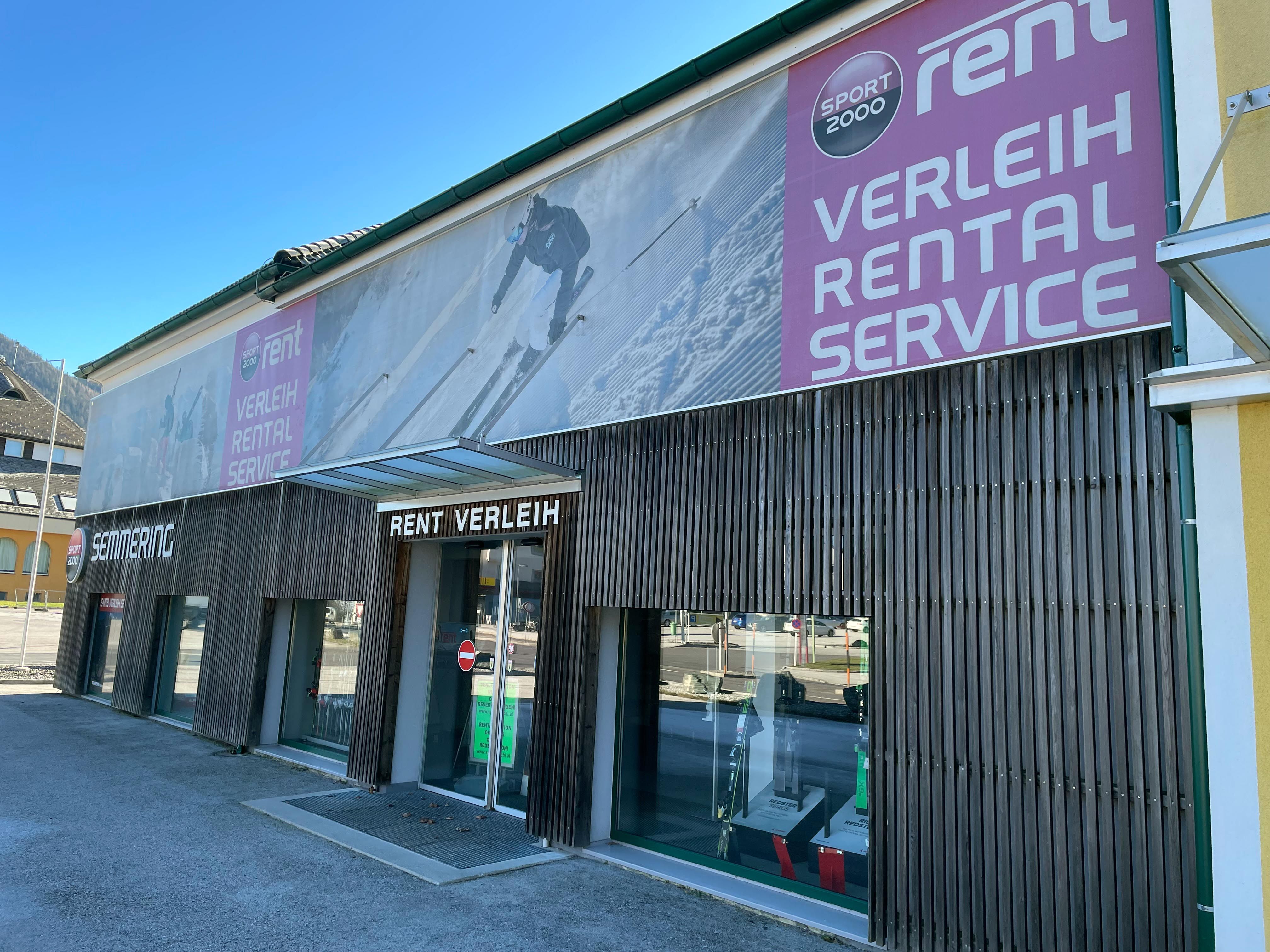 Exterior view of a sports rental store with large advertising banners and shop windows.