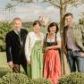 The Pichler family in traditional dress stand outside in front of a tree, with Sift Melk in the background