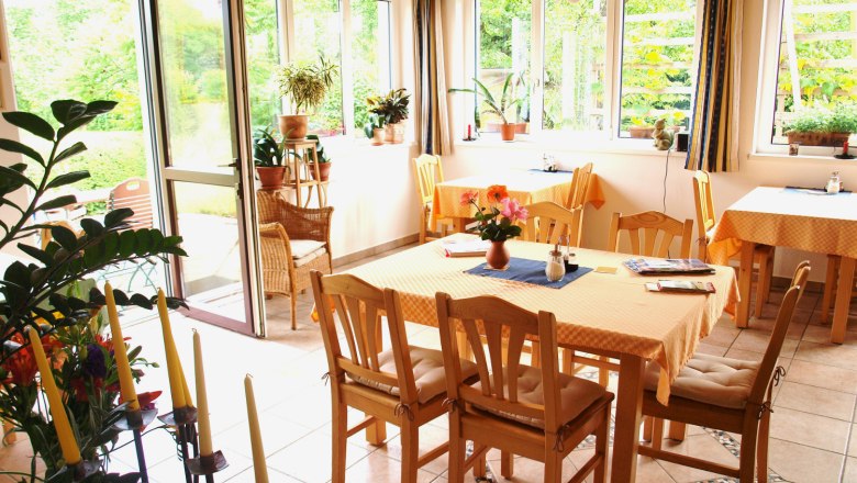 A bright conservatory with wooden furniture, plants and large windows that let in plenty of light.