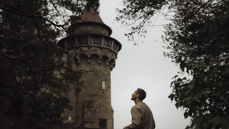 Man looking at Kreuzenstein Castle through trees.