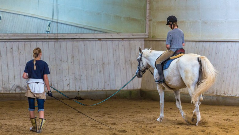 Riding lessons in an indoor arena with a white horse and two people.