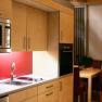 Modern kitchen with wooden cupboards, red splashback, microwave and dining table in the background.