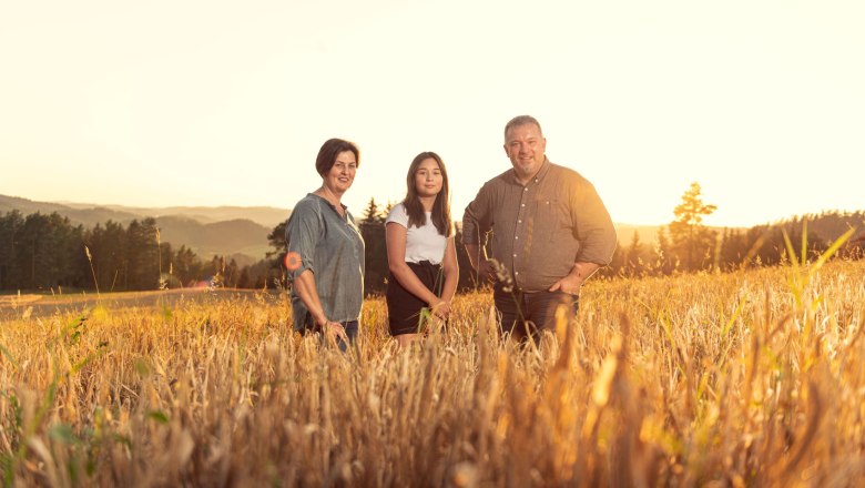 Three people stand in a field at sunset.