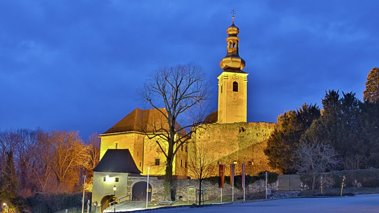 Illuminated Gloggnitz Castle at dusk with a blue sky.