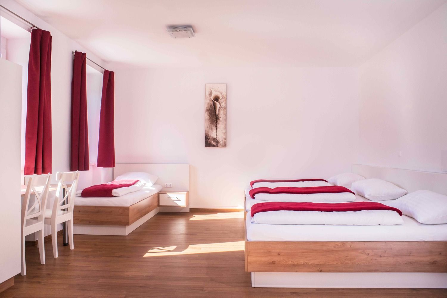 Bright room with two beds, red curtains and a picture on the wall.