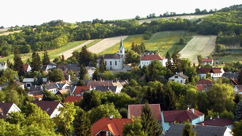 Landscape with church and village in the foreground, surrounded by fields and hills.