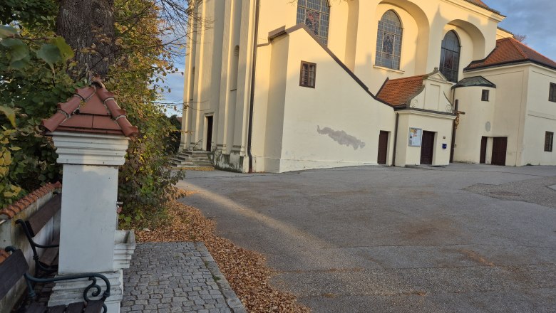 Church with a yellow fa&ccedil;ade and red roofs, surrounded by autumn leaves and trees.