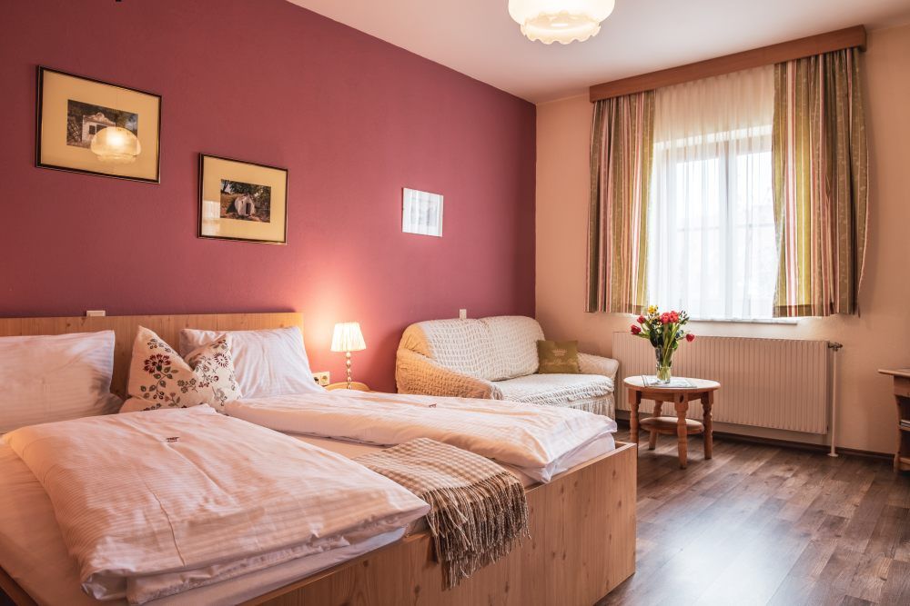 Cozy guest room with double bed, sofa, table and bouquet of flowers.