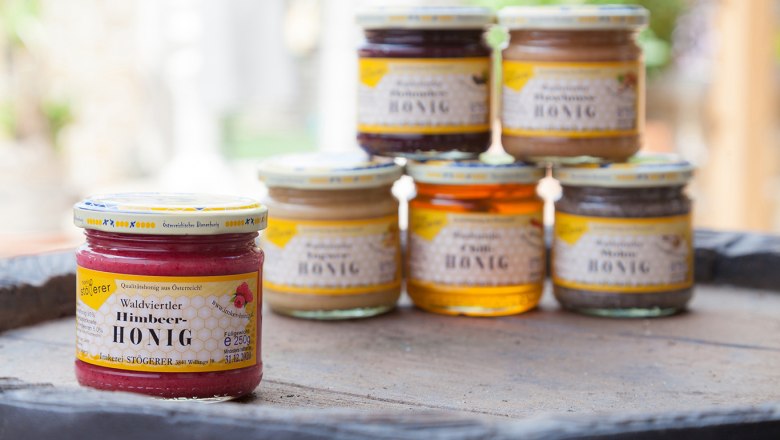 Various jars of honey on a table, raspberry honey in the foreground.
