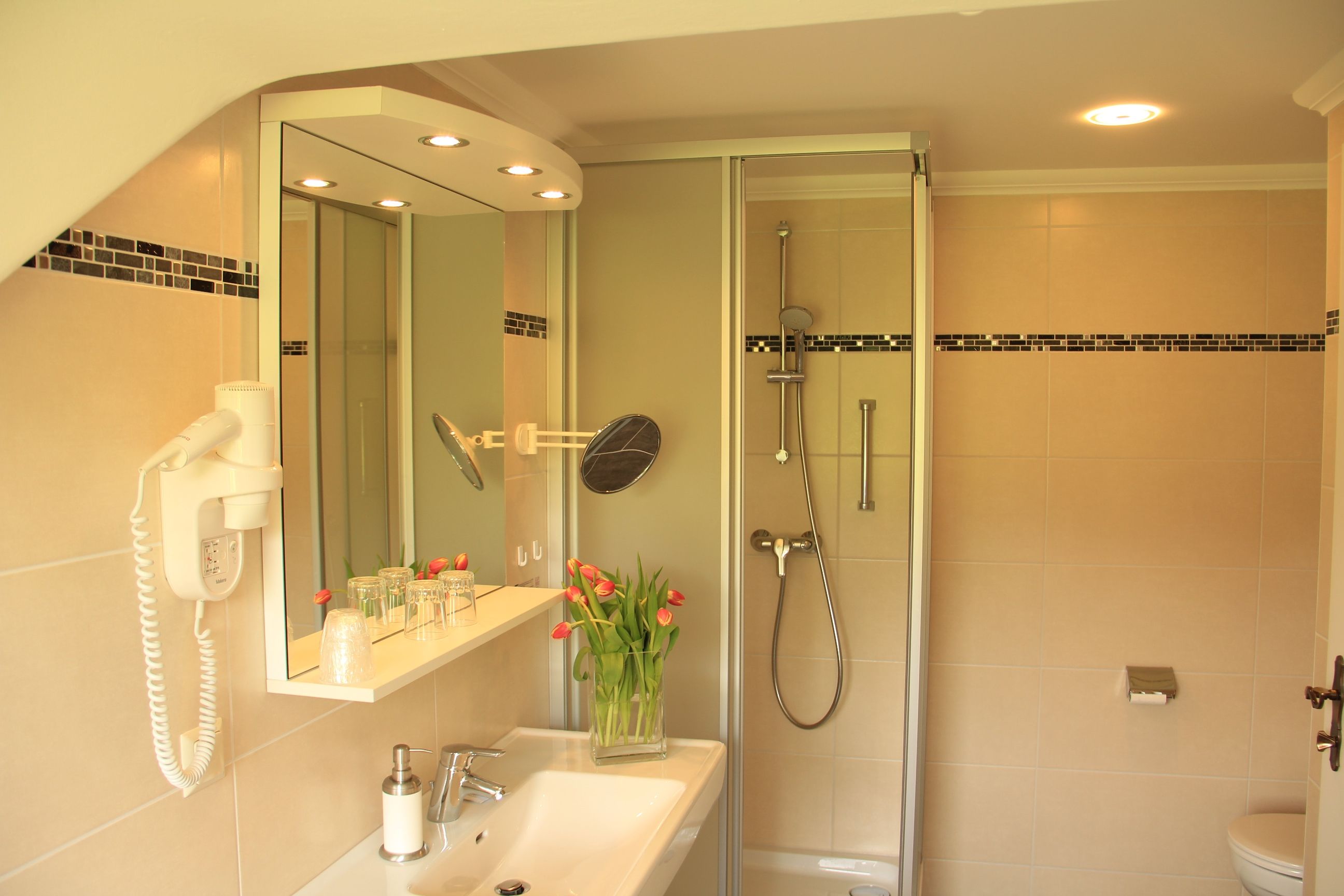 Modern bathroom with shower, washbasin, mirror and tulips.