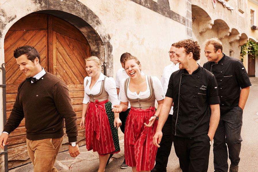 Group of people in traditional clothing and cooking uniforms in front of an old building.