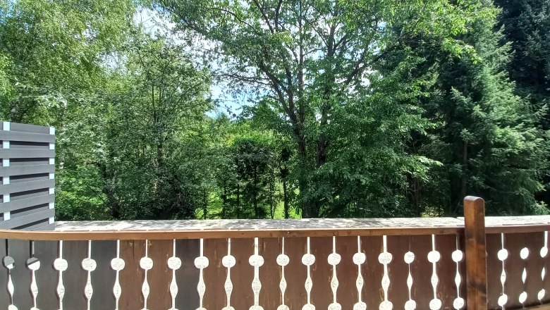 Wooden terrace with decorative railing and view of green trees in the background.