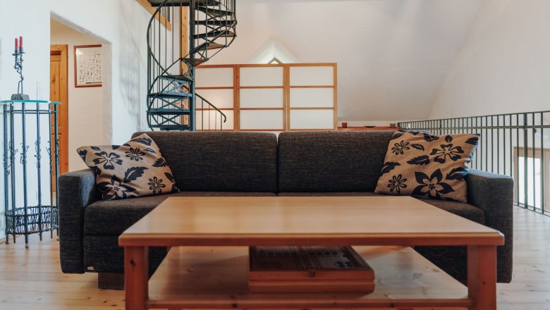 Living room with sofa bed, wooden table and spiral staircase in a loft.
