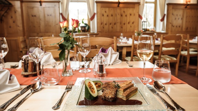 An elegantly laid table in a rustic restaurant with a plate of gourmet food, wine glasses and a vase of roses.