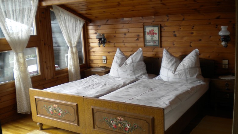 Cozy bedroom with wooden walls, double bed and lace curtains.