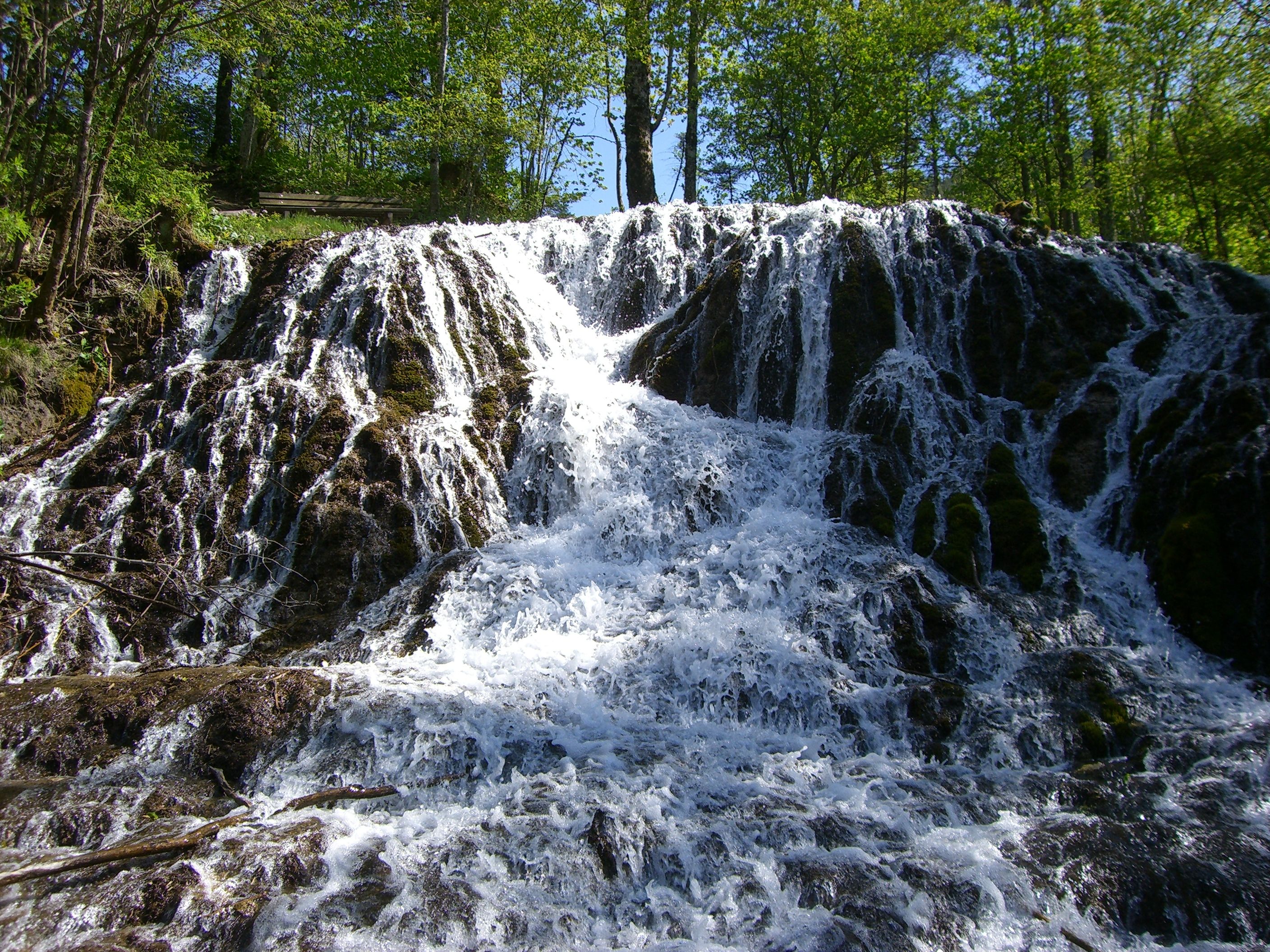 A waterfall flows over moss-covered rocks in a forest.